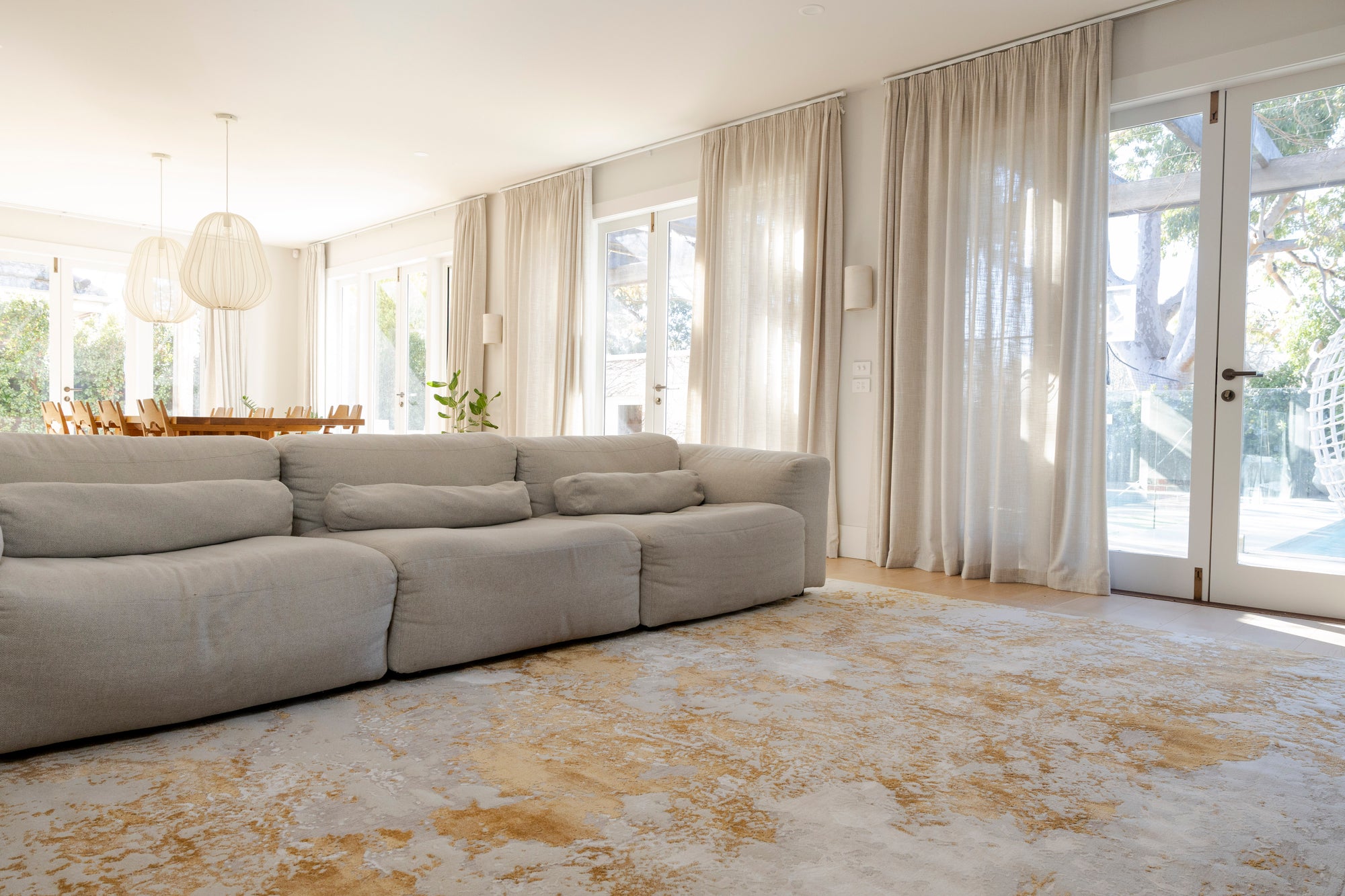 Large sectional sofa in a living room with light-coloured curtains and Golden Dusk Abstract Rug by Four Corners Rugs