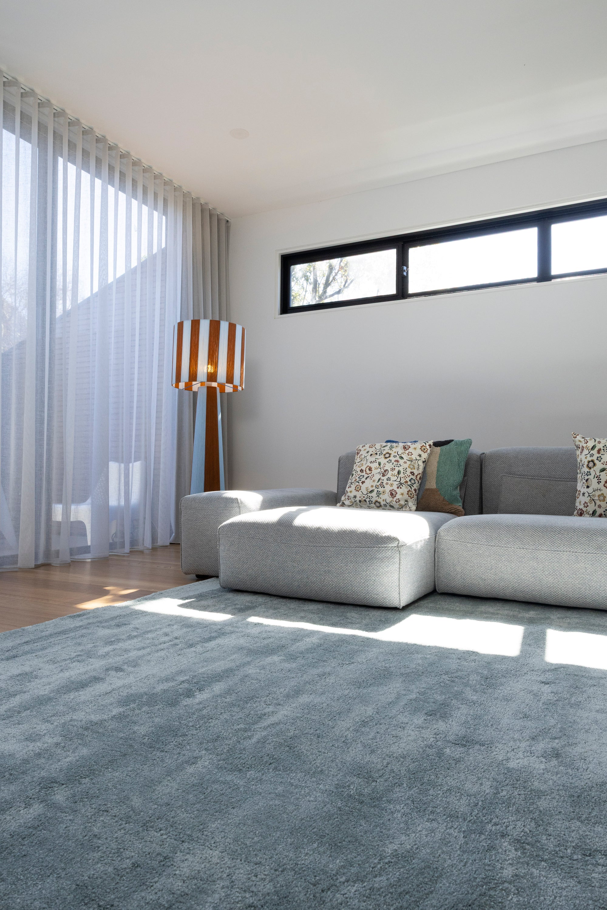 Modern living room with a grey sectional sofa, patterned cushions, a striped lamp and Plush Ice Blue Rug by Four Corners Rugs