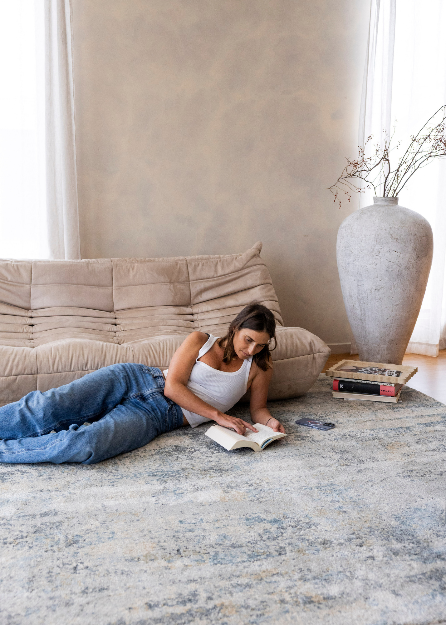 Woman reading a book on a rug in a living room with a beige sofa and large vase on Cooper Plush Rug by Four Corners Rugs