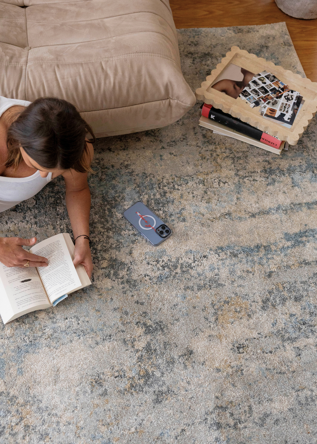 Person reading a book on Cooper Plush Rug by Four Corners Rugs with a photo frame and phone nearby.
