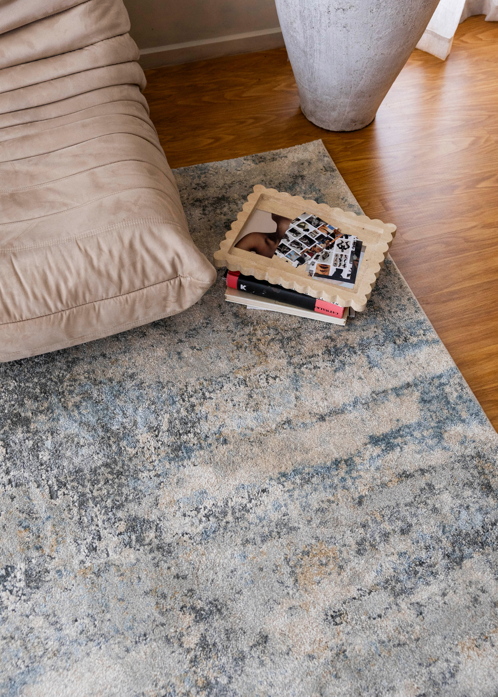 Cooper Plush Rug by Four Corners Rugs with a pillow and books on top, next to a beige couch.