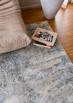Cooper Plush Rug by Four Corners Rugs with a pillow and books on top, next to a beige couch.