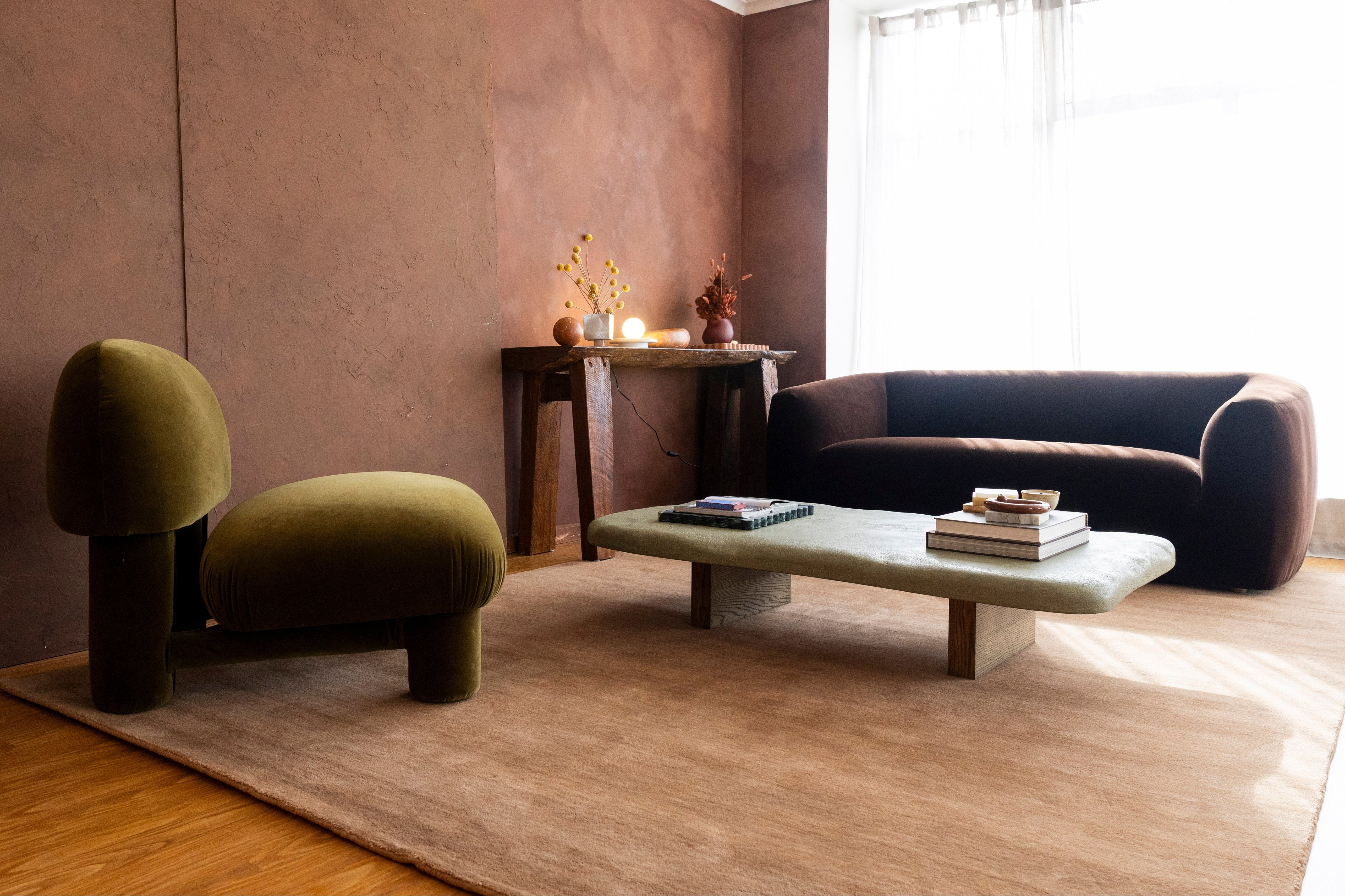 A modern living room setup featuring a mushroom-shaped olive green chair, a dark brown sofa, again a textured brown wall and on the Texture Wool Rug Teddy Brown by Four Corners Rugs