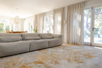 Large sectional sofa in a living room with light-coloured curtains and Golden Dusk Abstract Rug by Four Corners Rugs