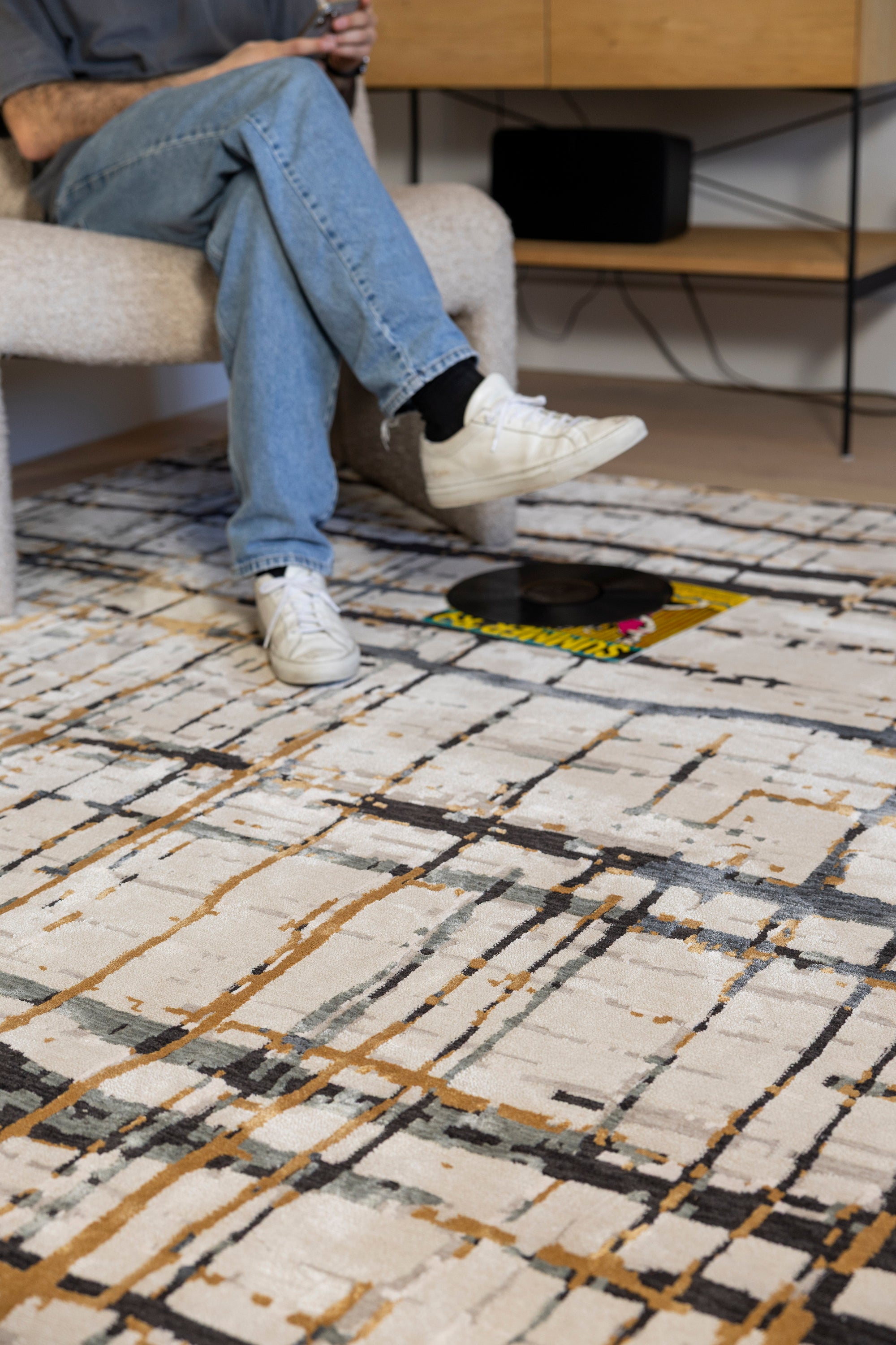 Person sitting on a chair with feet on a Moonlit Bloom Abstract Rug by Four Corners Rugs in a room with a record