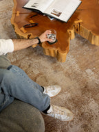 Person sitting on a couch with a glass of water next to a wooden table on Nude Contrast Gold and Brown Rug By Four Corners Rugs