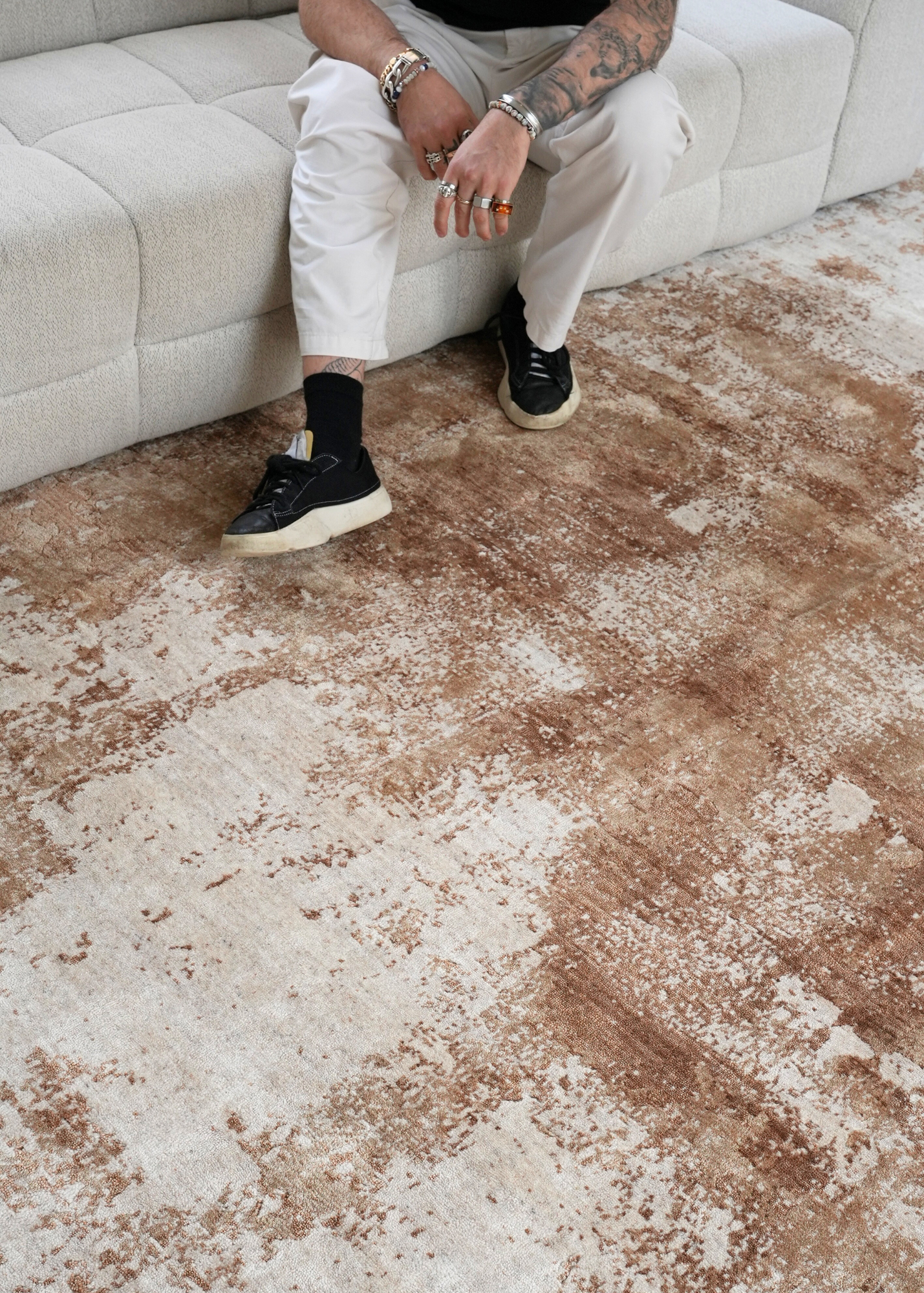 Person sitting on a white couch with Nude Contrast Gold and Brown Rug By Four Corners Rugs