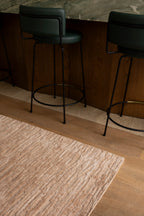 Two green bar stools against a wooden wall with Oceana Dusty Rose by Four Corners Rugs
