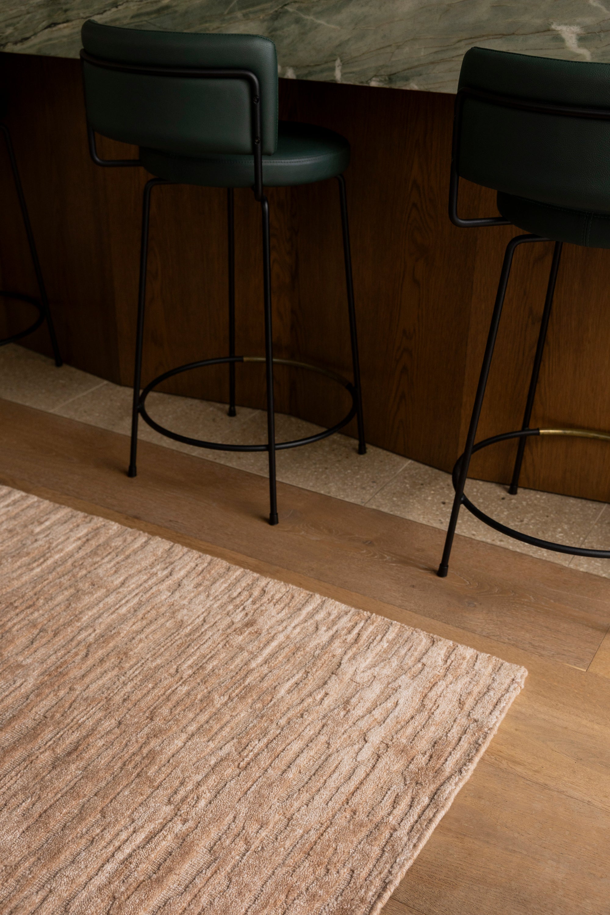Two green bar stools against a wooden wall with Oceana Dusty Rose by Four Corners Rugs