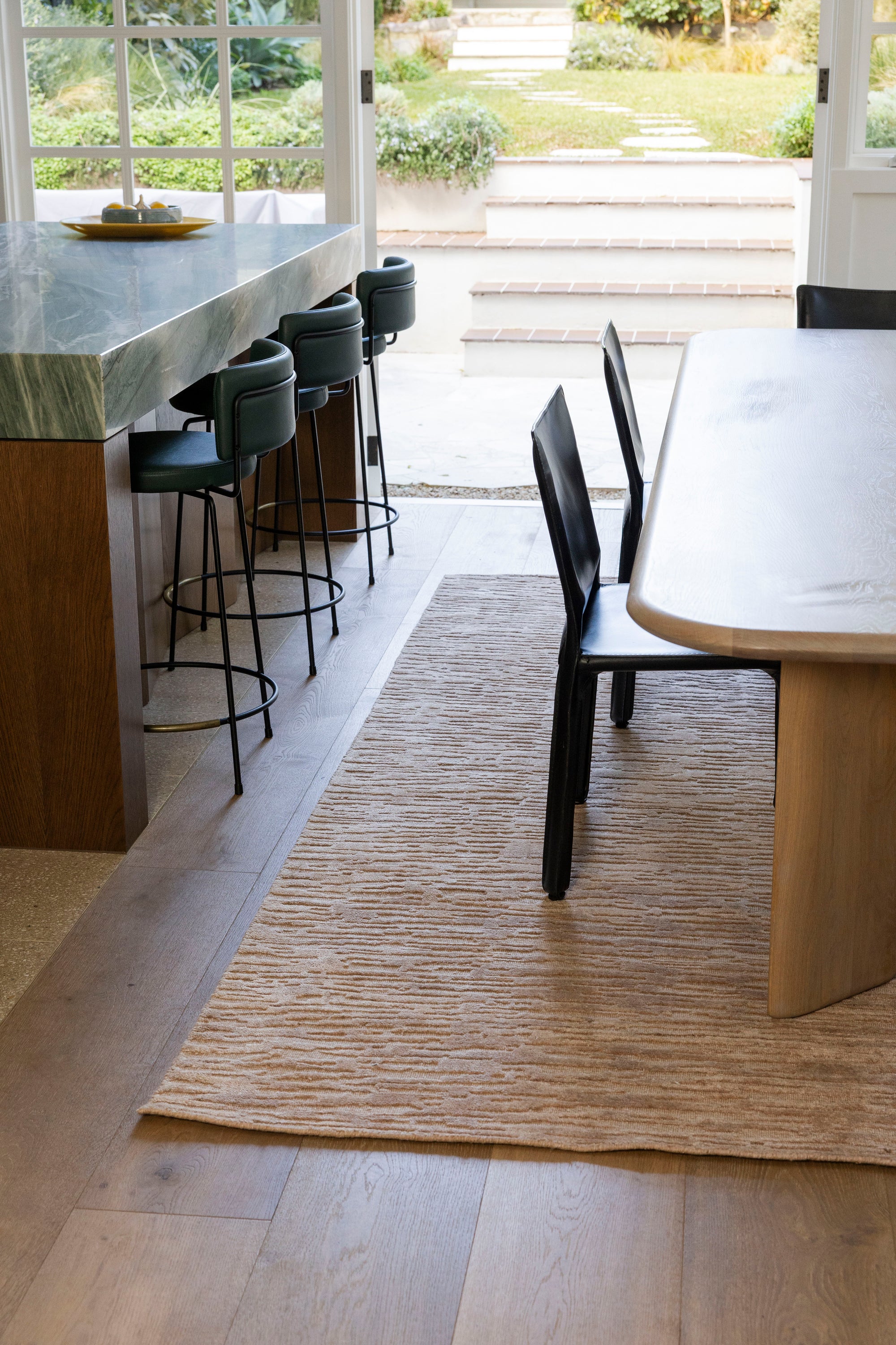 Modern kitchen with island, stools, and dining table on a wooden floor and Oceana Dusty Rose by Four Corners Rugs
