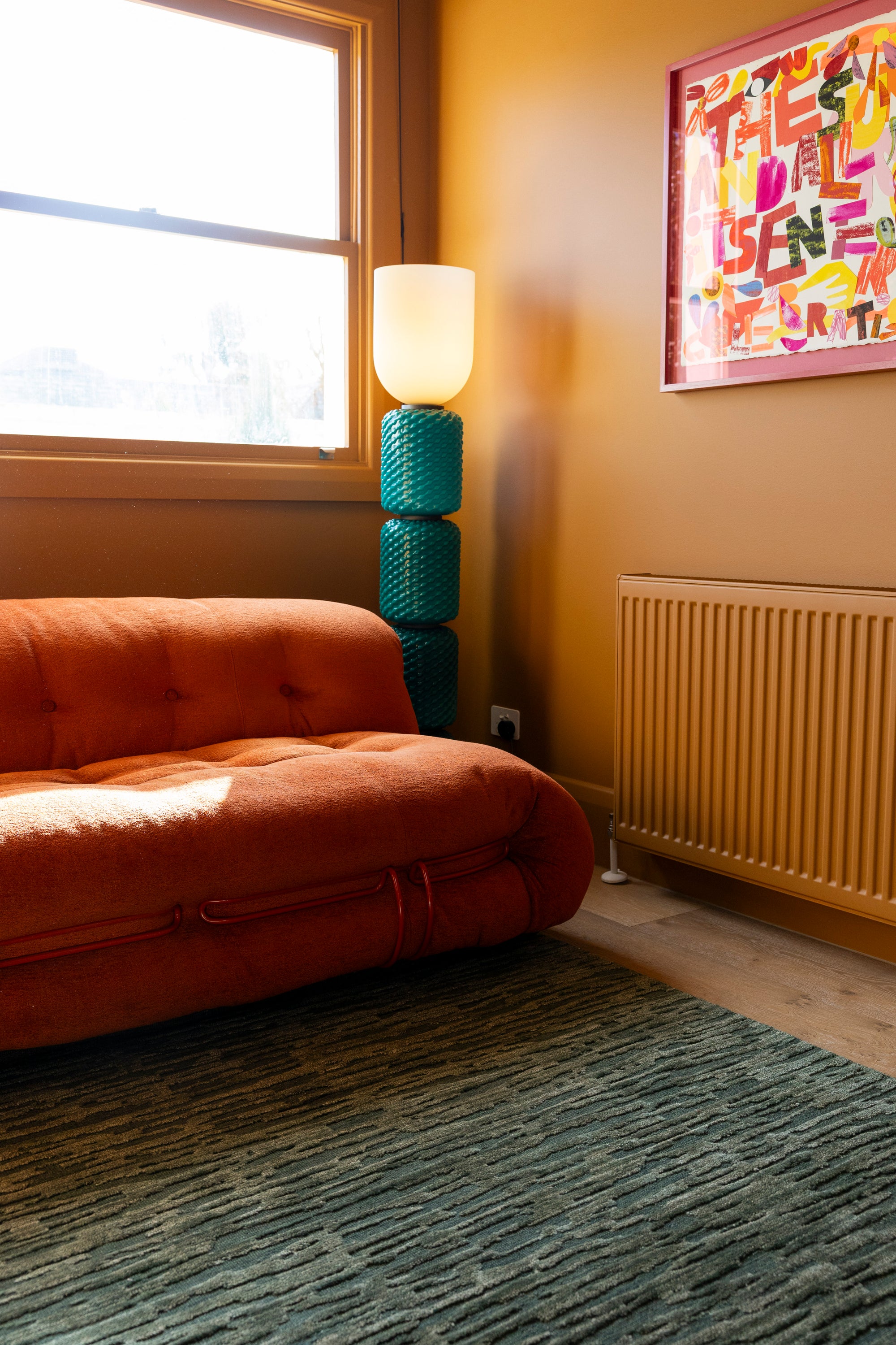 Living room with orange sofa, blue lamp, and colourful wall art on Oceana Forrest Green by Four Corners Rugs