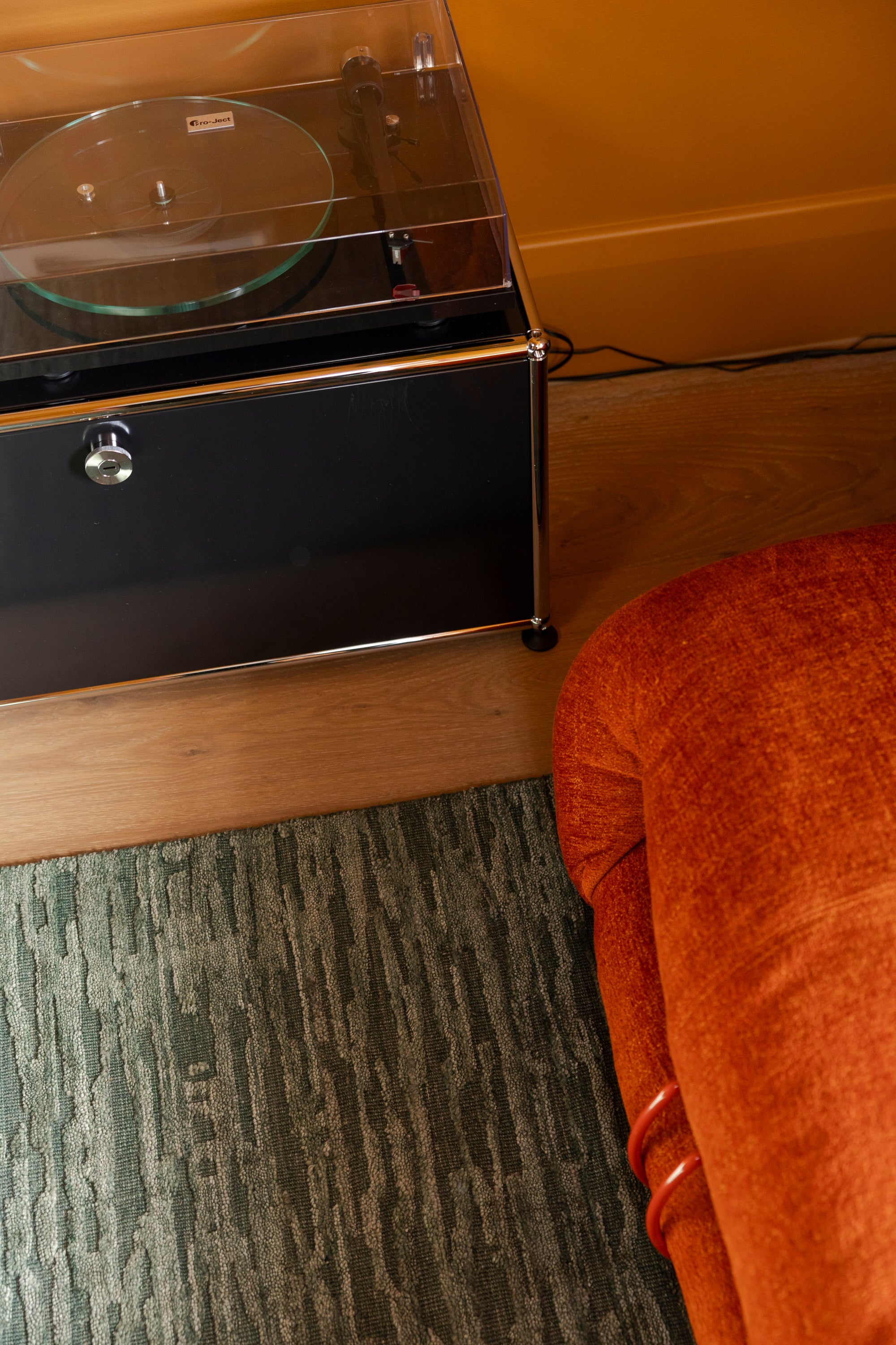 Small record player on a stand next to a orange chair on Oceana Forrest Green by Four Corners Rugs