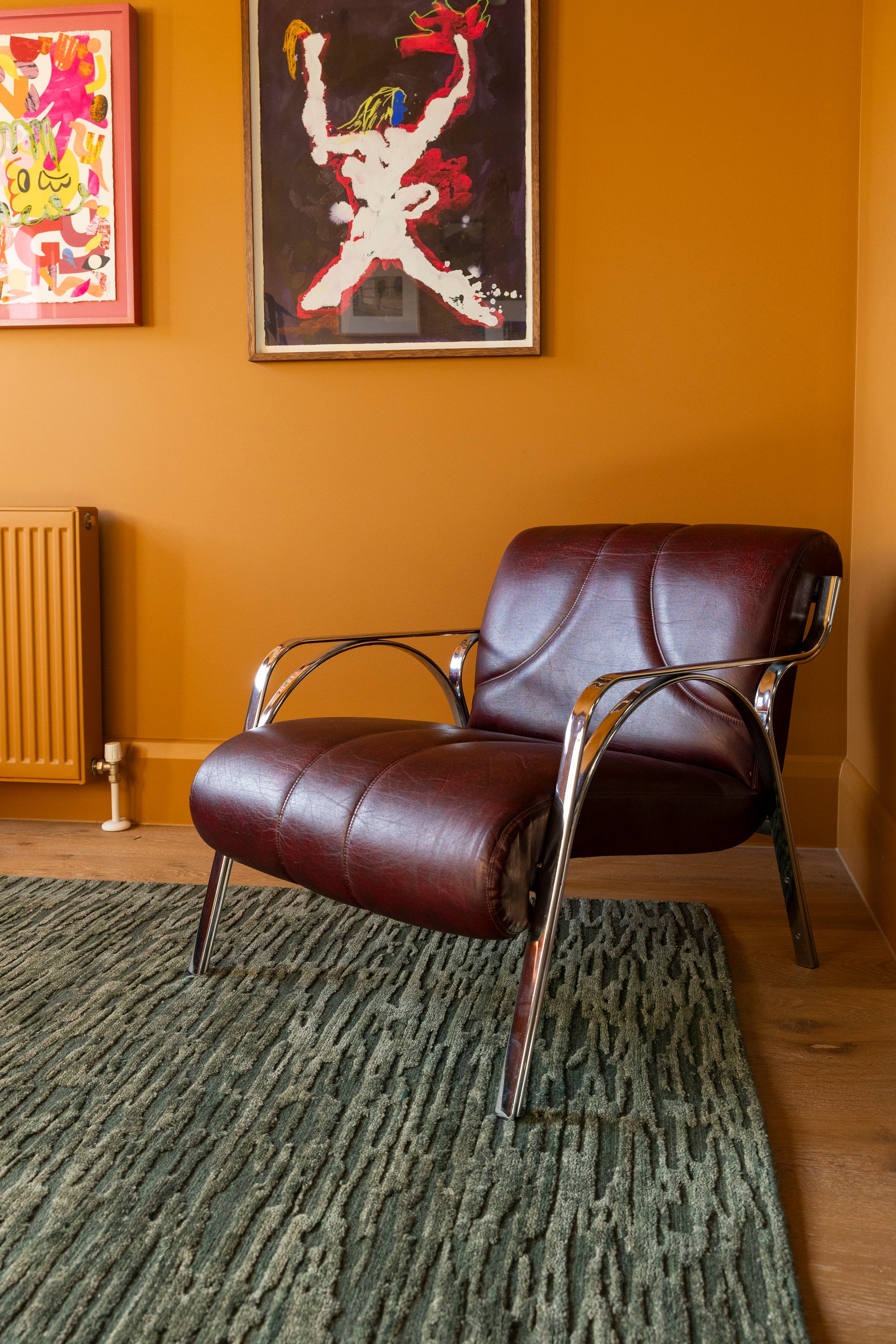 Brown leather armchair in a room with orange walls and abstract art on Oceana Forrest Green by Four Corners Rugs