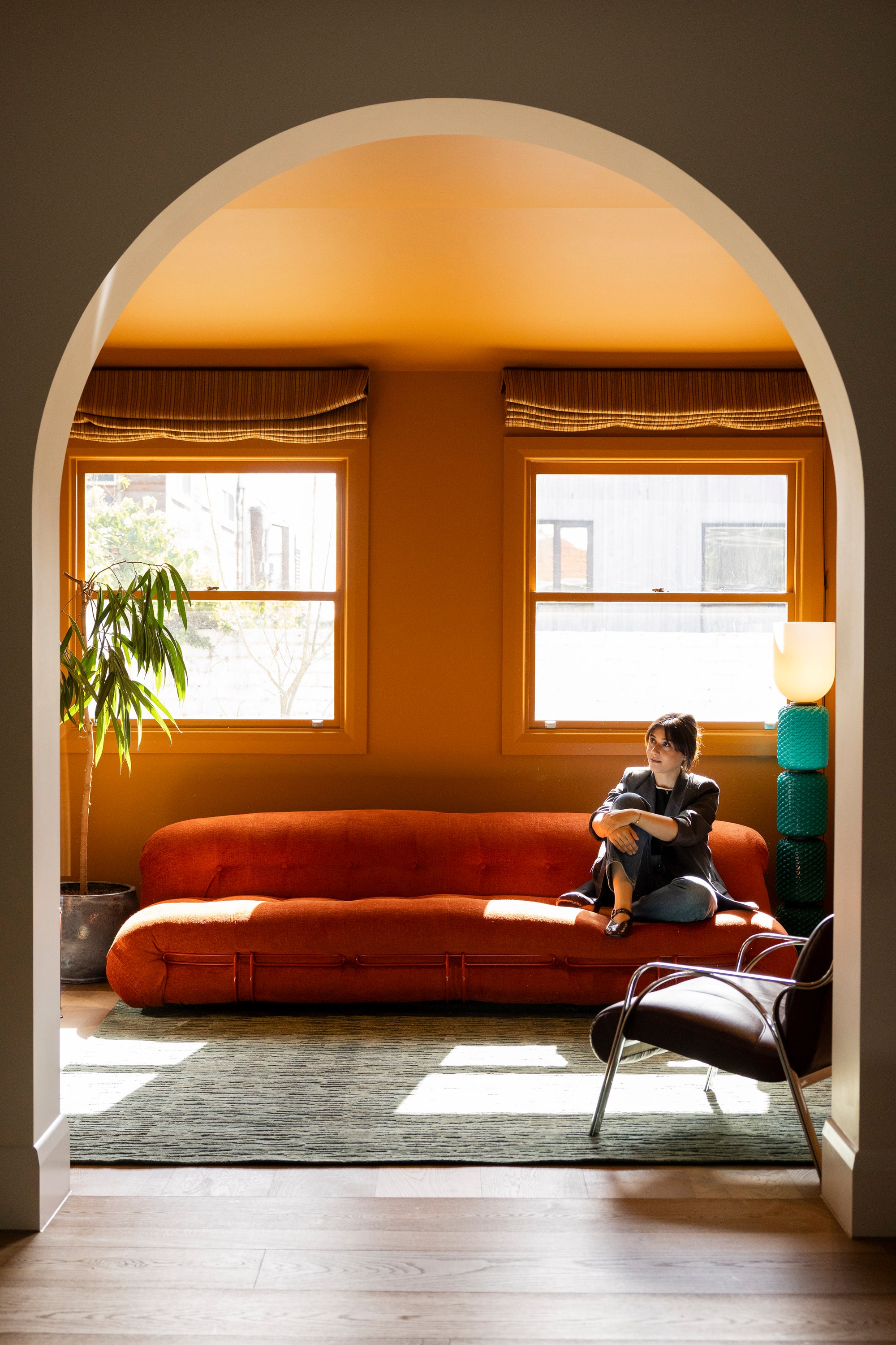 Talla sitting on a red sofa in a sunlit room on Oceana Forrest Green by Four Corners Rugs