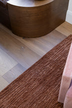 Oceana Rust by Four Corners Rugs on a wooden floor with a wooden side table.