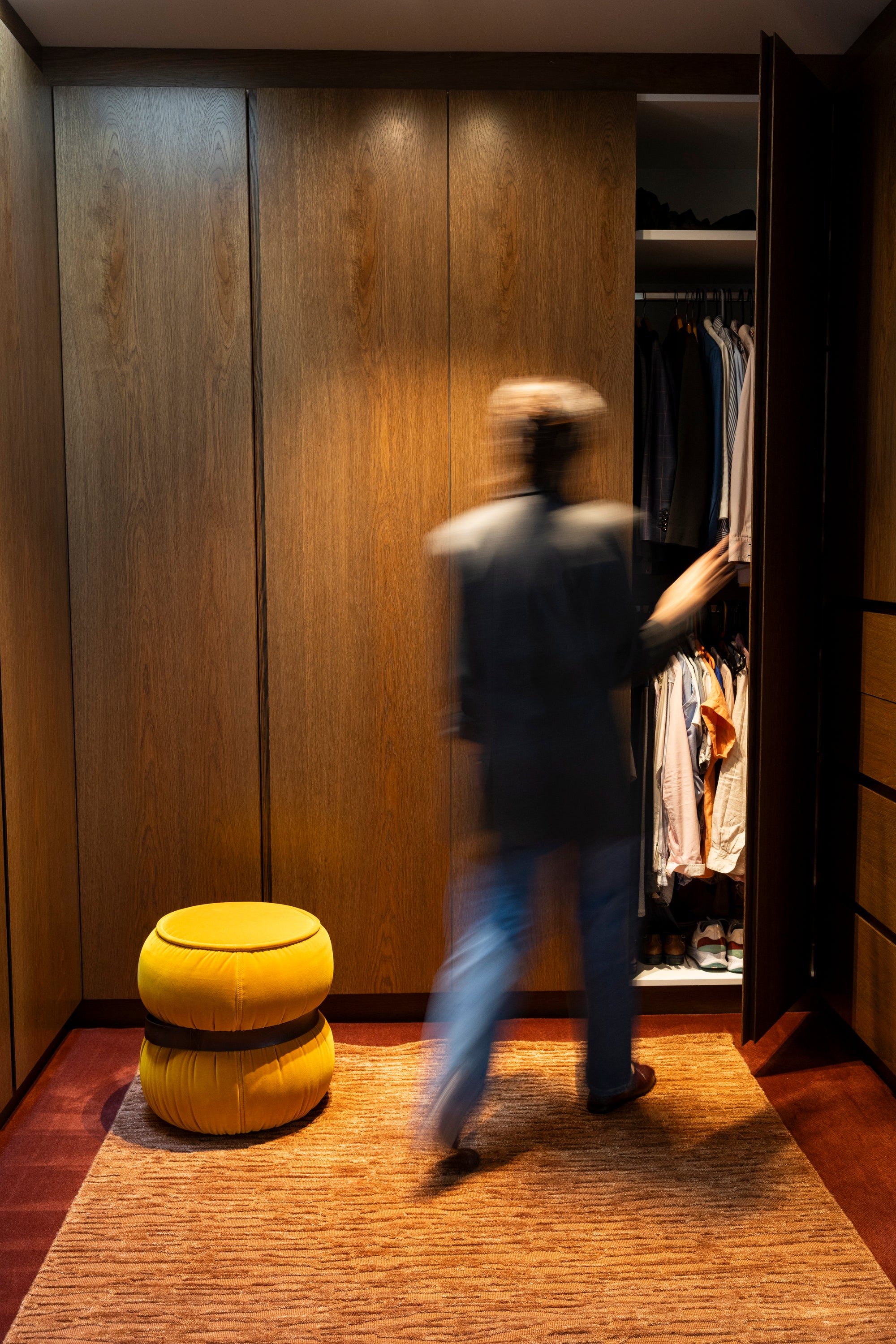 Person walking into a walk-in wardrobe on Oceana Rust by Four Corners Rugs with a yellow ottoman