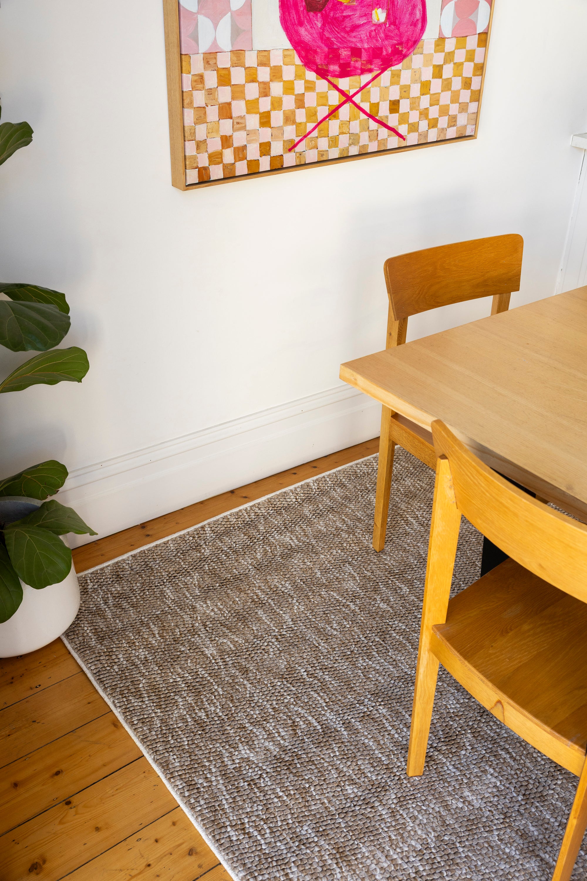 Dining area with wooden table and chairs on Pebbles Beige by Four Corners Rugs, colourful abstract art on the wall.
