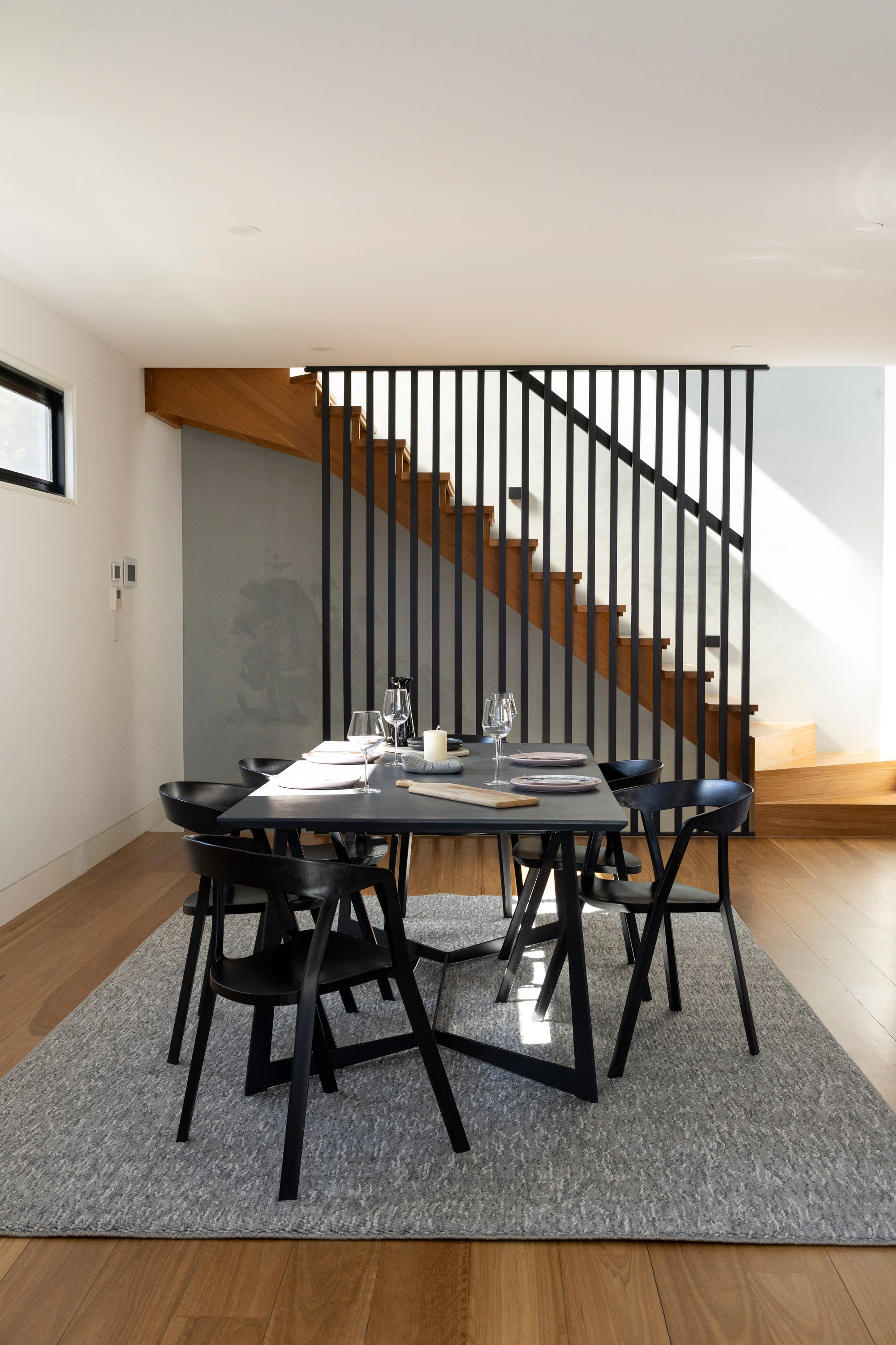 Dining area with black table and chairs on Pebbles Light Grey by Four Corners Rugs, staircase in the background.