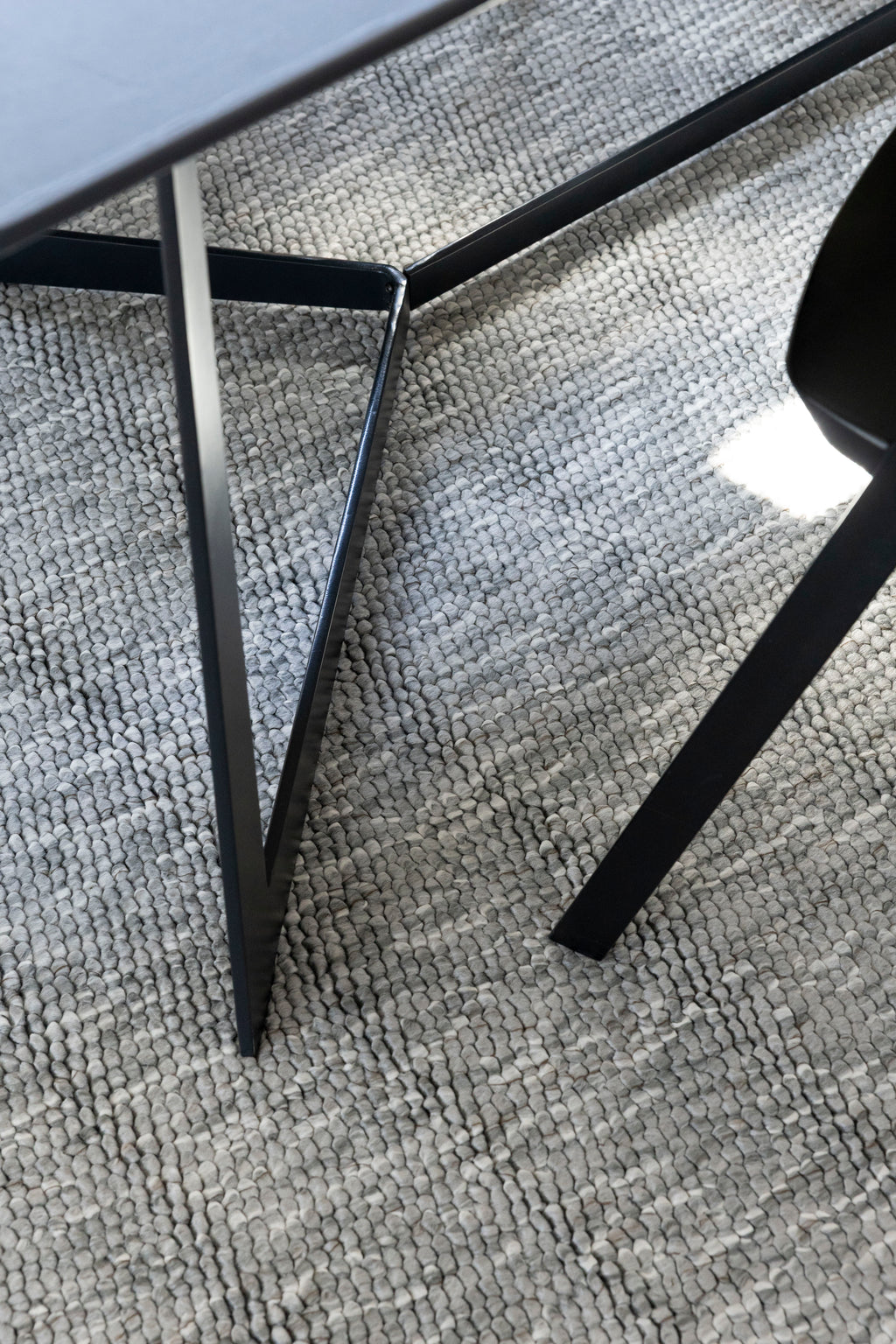 Close-up of a black chair leg on Pebbles Light Grey by Four Corners Rugs