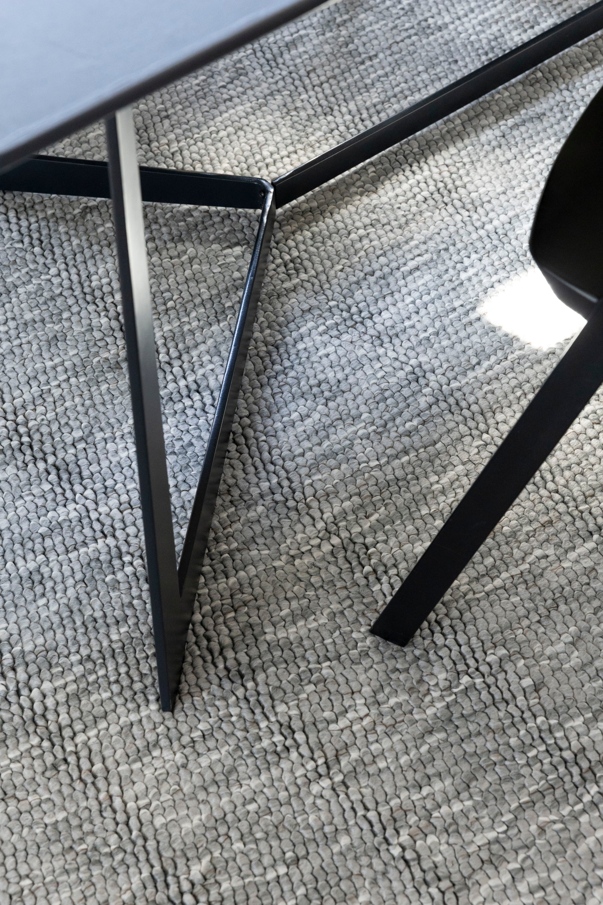 Close-up of a black chair leg on Pebbles Light Grey by Four Corners Rugs