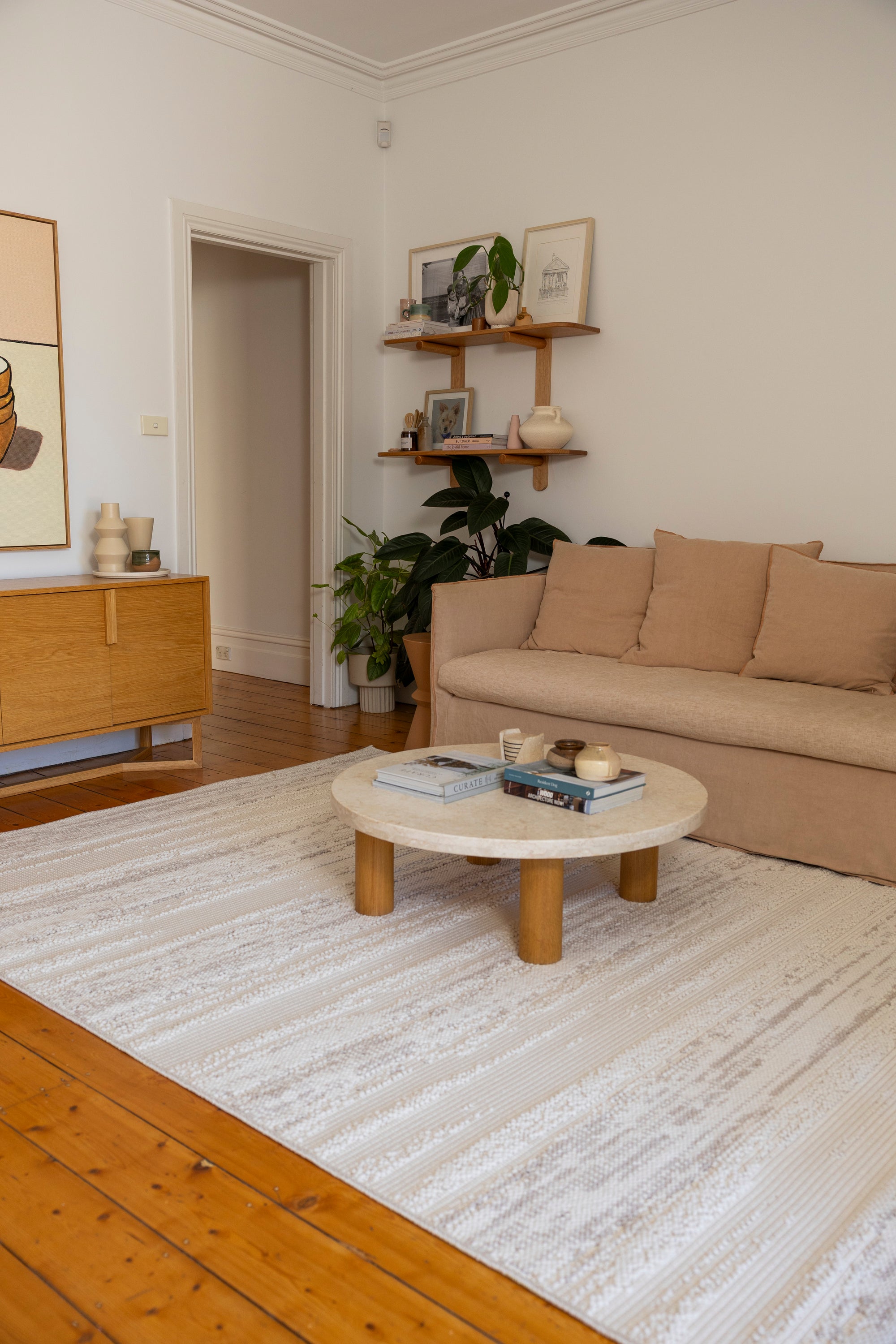 Living room with beige sofa, wooden coffee table, and shelves with decor on Pebbles White Rug by Four Corners Rugs
