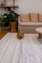 Dog sitting on Pebbles White Rug by Four Corners Rugs in a living room with a beige sofa and plant.