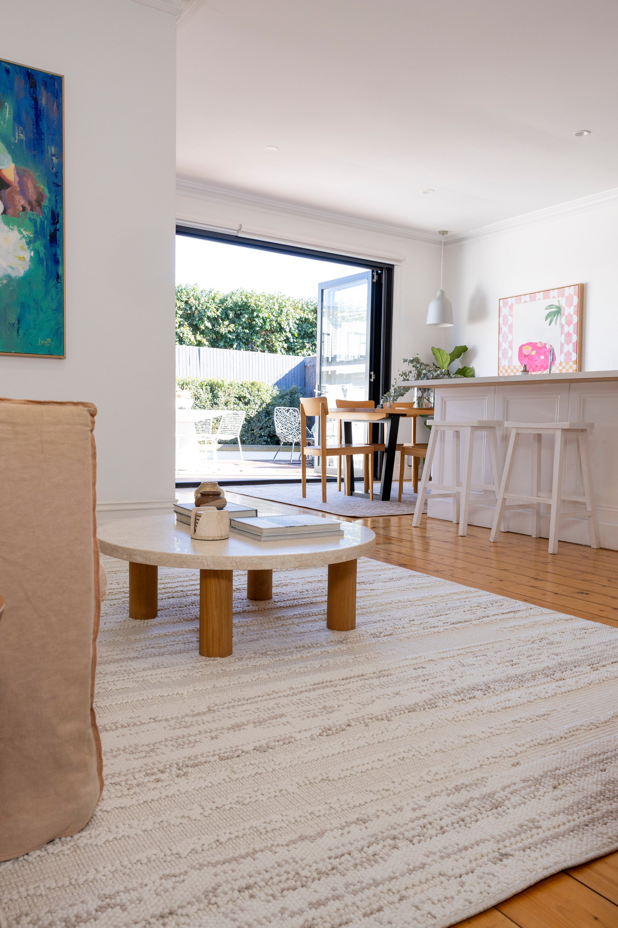 Modern living room with a round wooden coffee table, beige sofa, large windows and Pebbles White Rug by Four Corners Rugs