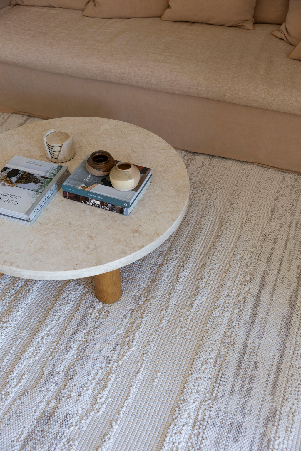 Round stone coffee table with decorative items on Pebbles White Rug by Four Corners Rugs in a living room setting.