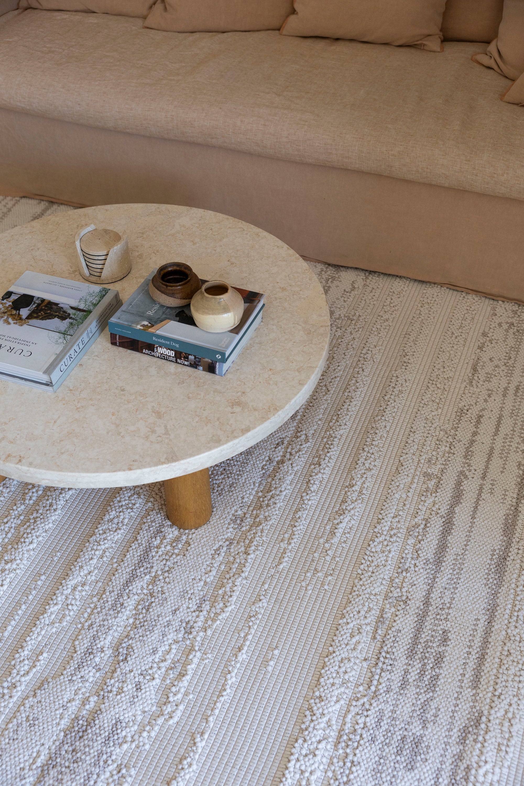 Round stone coffee table with decorative items on Pebbles White Rug by Four Corners Rugs in a living room setting.