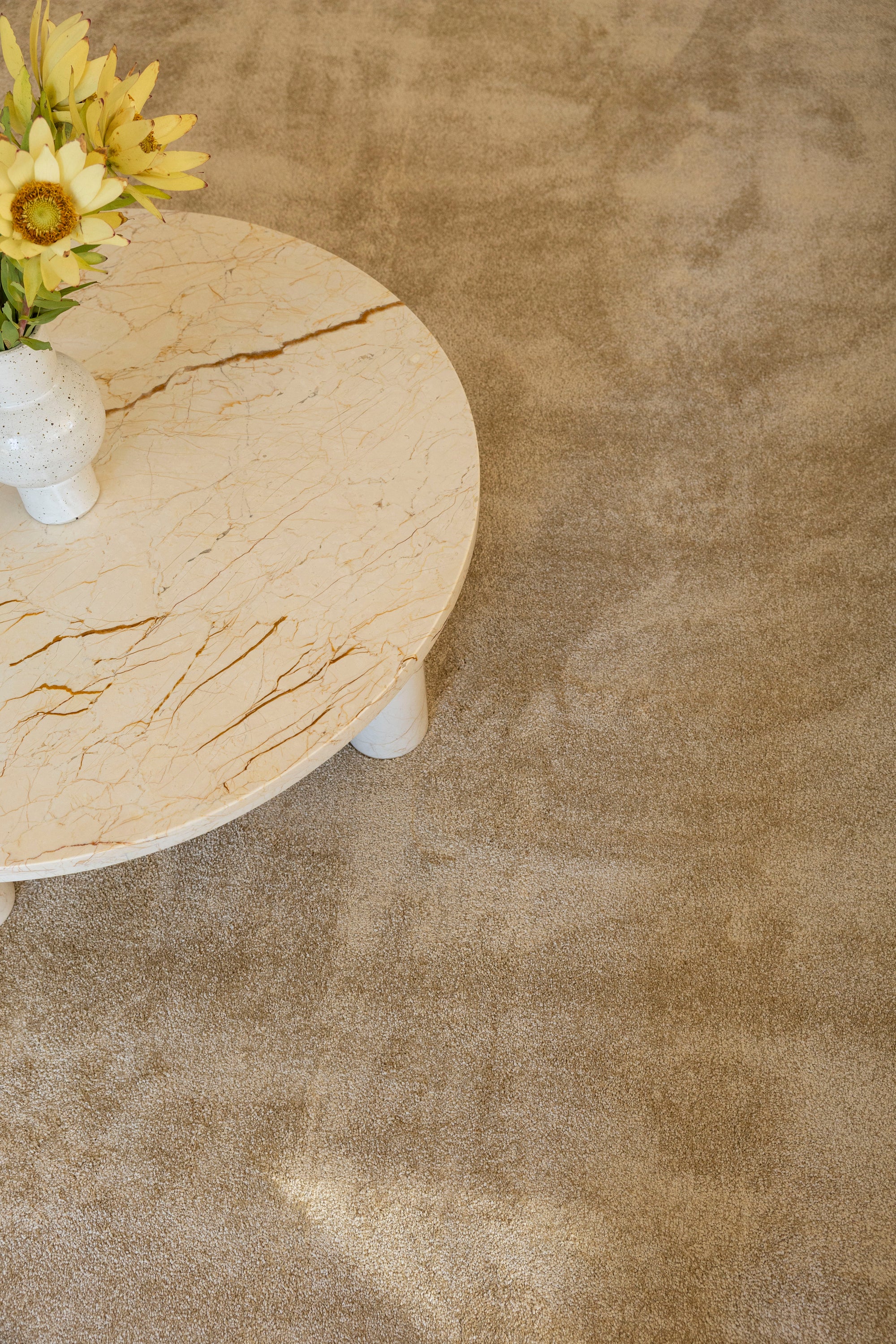 Round wooden table with a vase of yellow flowers on Plush Gold Rug by Four Corners Rugs