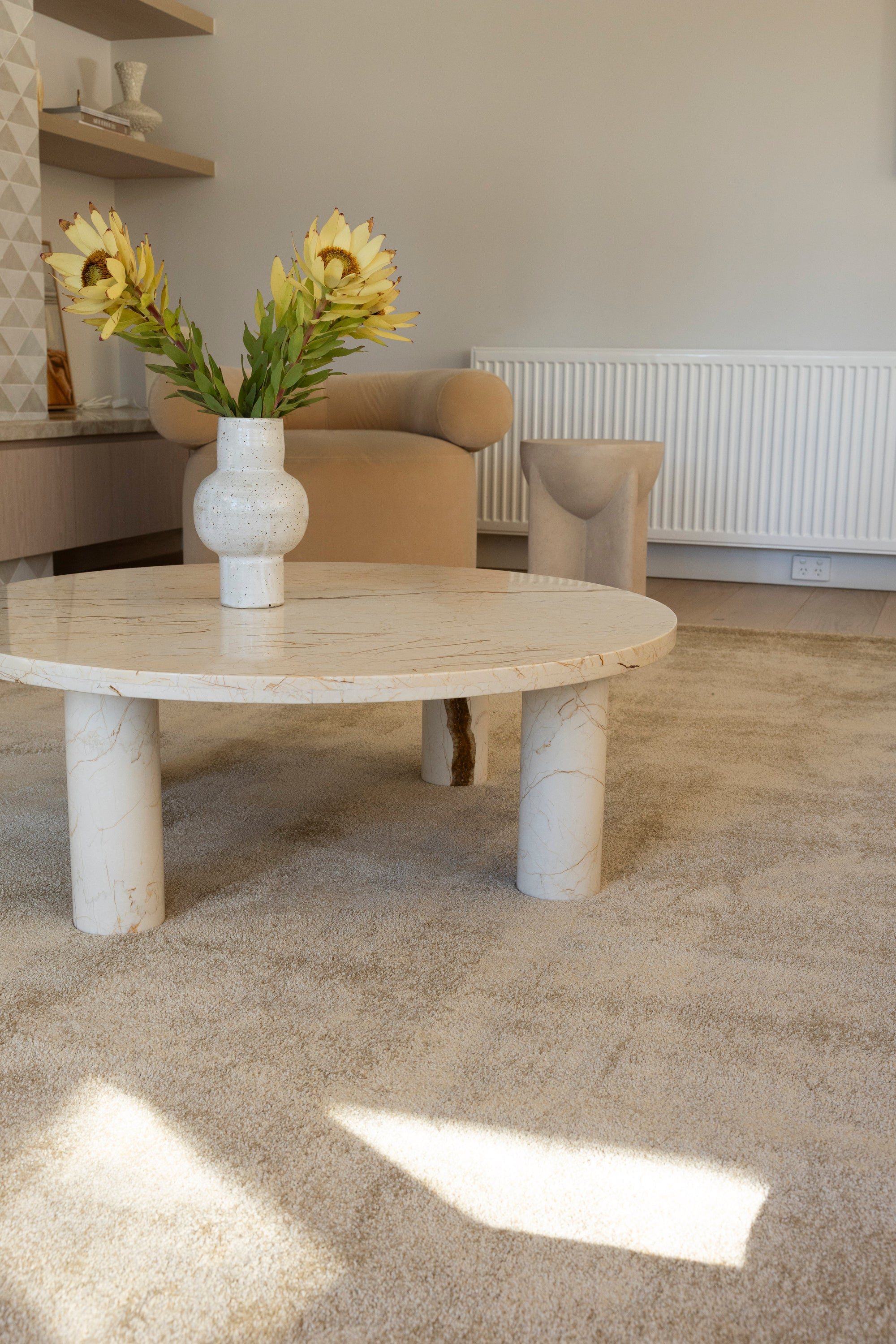 Round stone table with a vase of flowers in a living room setting and Plush Gold Rug by Four Corners Rugs