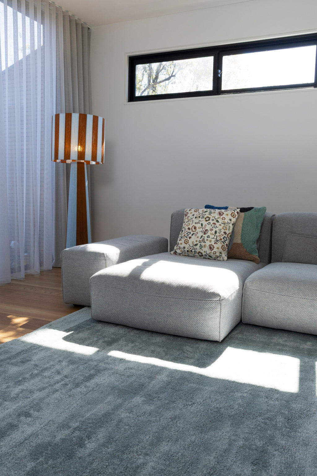 Modern living room with a grey sofa, patterned cushions, a striped floor lamp and Plush Ice Blue Rug by Four Corners Rugs