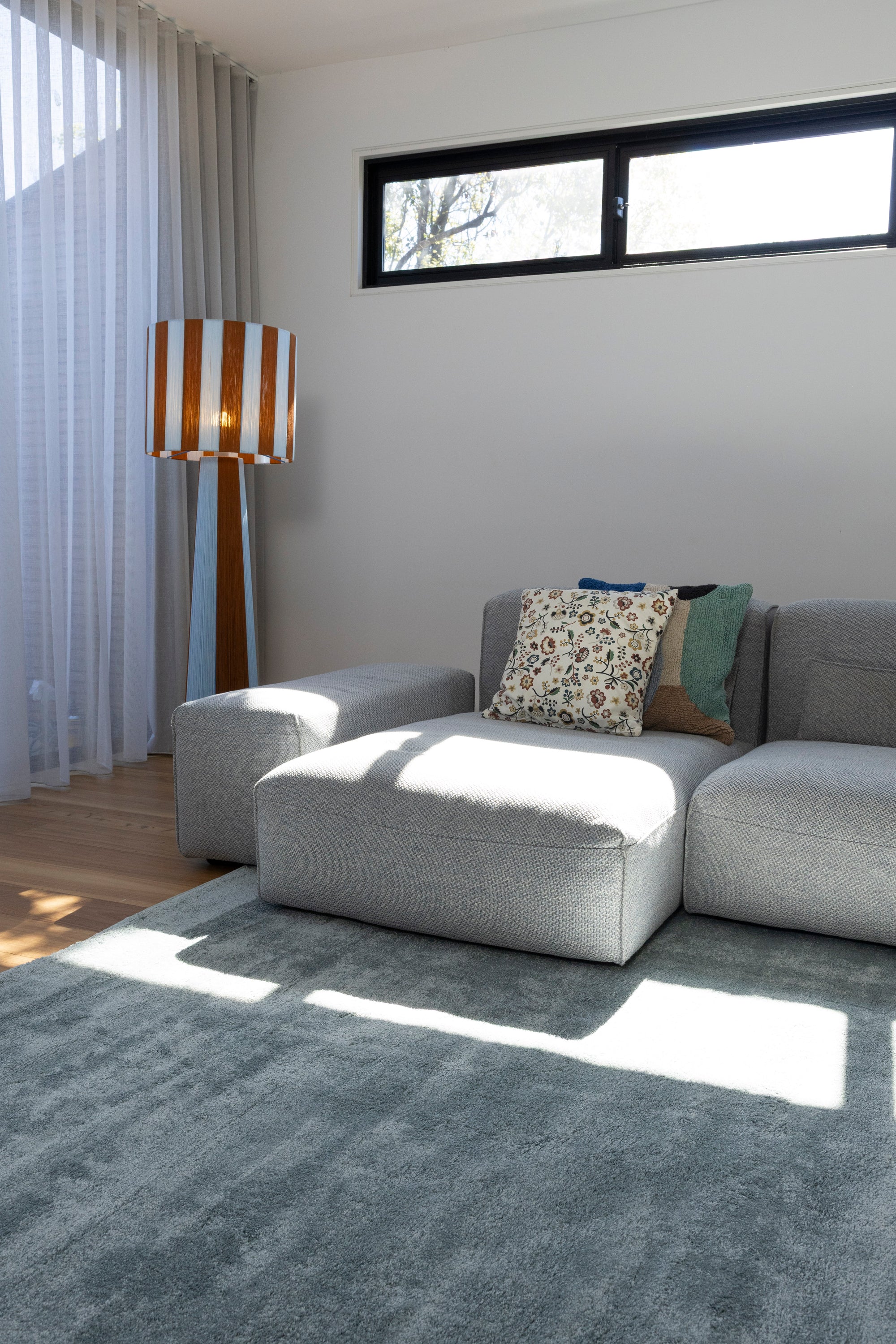 Modern living room with a grey sofa, patterned cushions, a striped floor lamp and Plush Ice Blue Rug by Four Corners Rugs