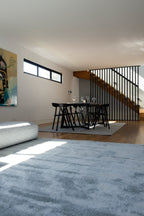 Open plan living with dining table on Pebbles Light Grey Rug by Four Corners Rugs and living room with Plush Ice Blue Rug by Four Corners Rugs