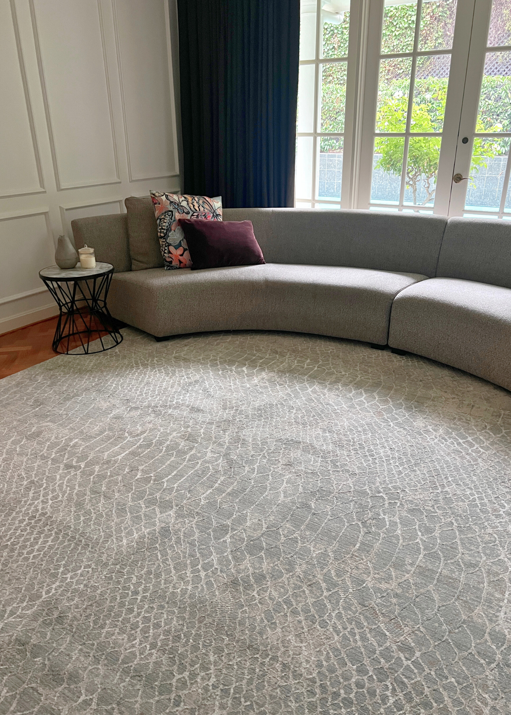 Grey sectional sofa with decorative pillows in a room with large windows on Python Blue Base Rug