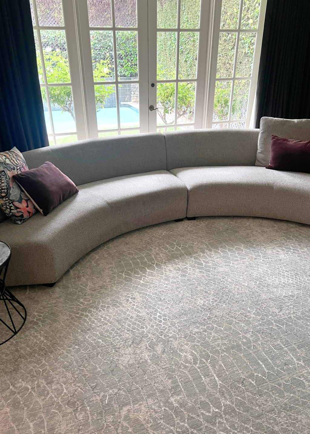 Curved beige sofa with decorative pillows in a living room with large windows and Python Blue Base Rug by Four Corners Rugs