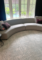 Curved beige sofa with decorative pillows in a living room with large windows and Python Blue Base Rug by Four Corners Rugs