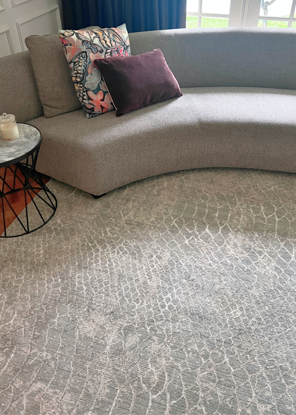 Gray textured carpet with a curved gray sofa and decorative pillows in the background on Python Blue Base Rug by Four Corners Rugs