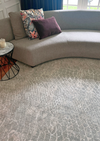 Gray textured carpet with a curved gray sofa and decorative pillows in the background on Python Blue Base Rug by Four Corners Rugs