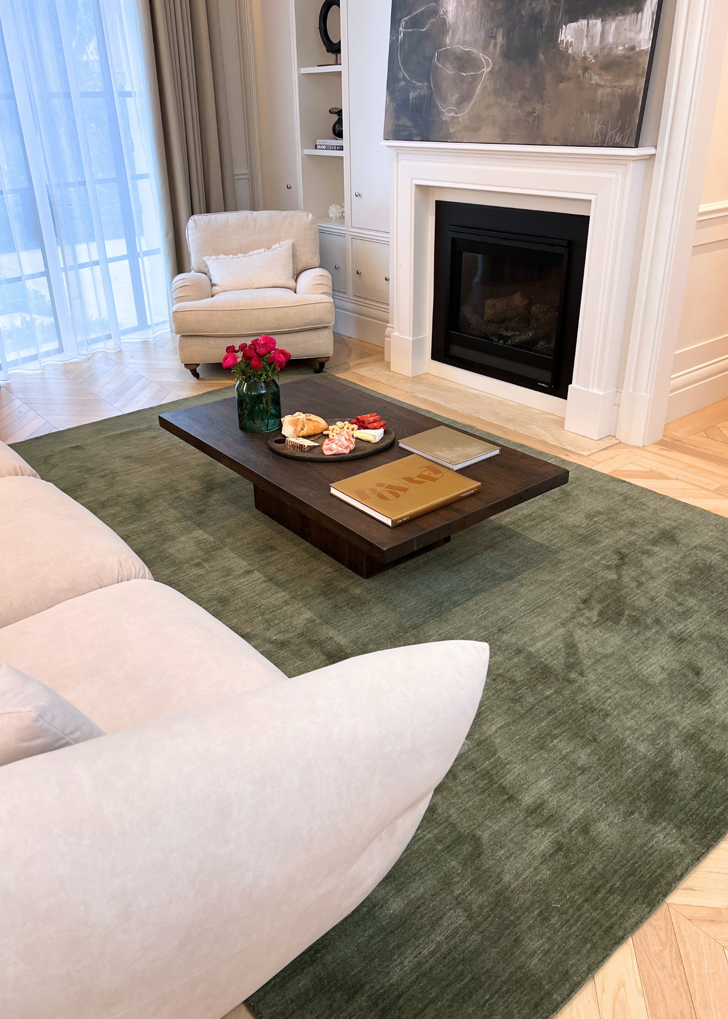 Living room with a Texture Wool Green Rug Handmade, white sofa, coffee table with items, and fireplace.