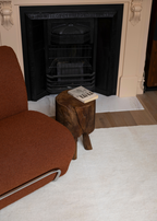 Burnt orange armchair next to a wooden stool with Wool Texture Milk Cream Rug